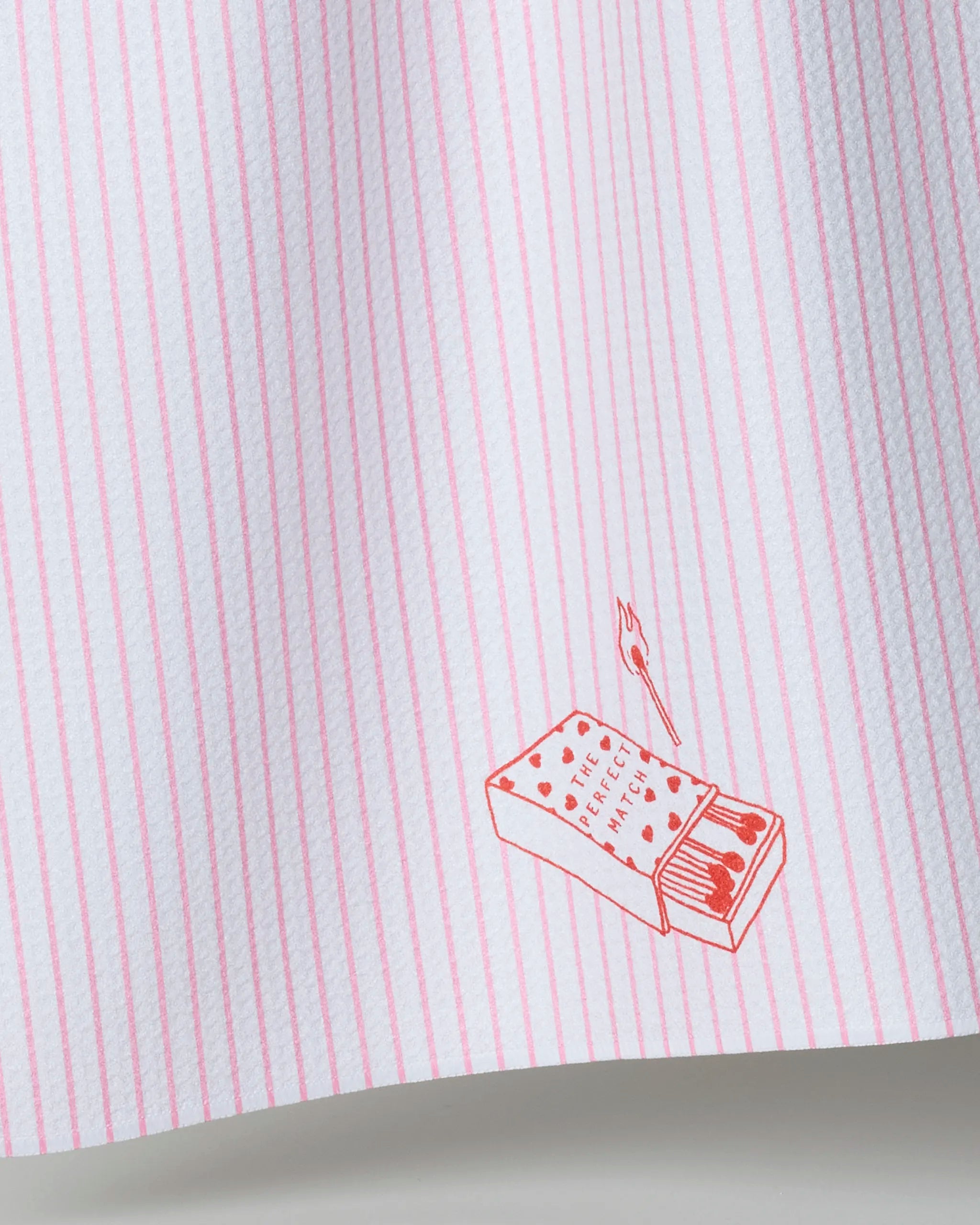 The Geometry Perfect Match white tea towel has thin pink stripes and a red illustration of an open matchbox with "THE PERFECT MATCH" and hearts—an ideal accent to brighten your kitchen décor.