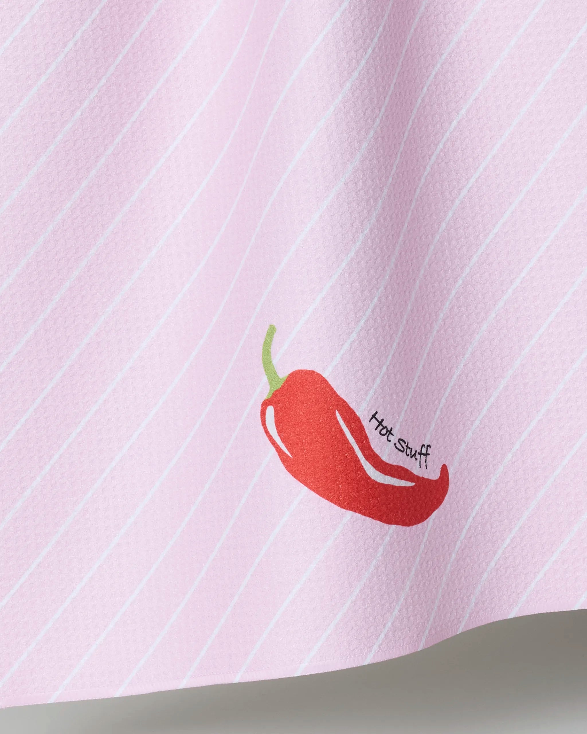 The Geometry “Hot Stuff” kitchen towel features thin white stripes on pink, a red chili pepper illustration, and the phrase "Hot Stuff," making it a fun and playful addition to your kitchen décor.