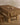 The Amber Stitch tablecloth by Geometry, brown and stain-resistant with a white cross pattern, covers a wooden table set with pears and a bowl. A wooden stool stands nearby on a light wood floor.