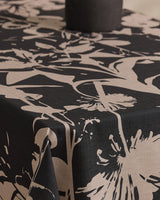 Close-up of a table covered with Geometrys Inverted Floral Black, a stain-resistant tablecloth featuring a bold beige floral design, topped with a round dark object.