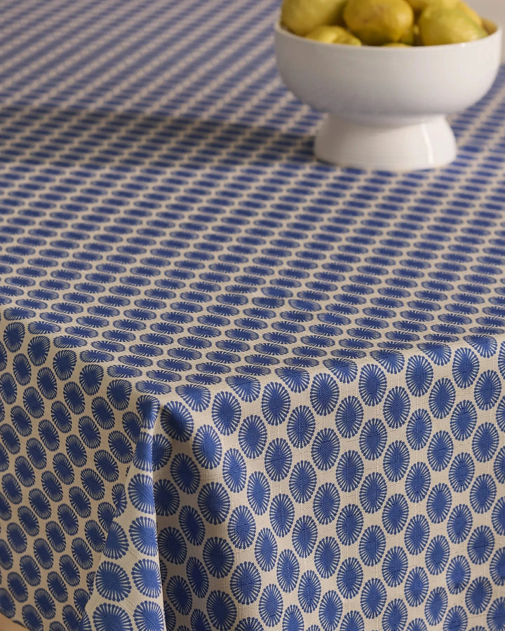 A table is draped with the Geometry Lagoon stain-resistant tablecloth, showcasing blue and white circular patterns, and a white bowl of pears sits near the top right corner.