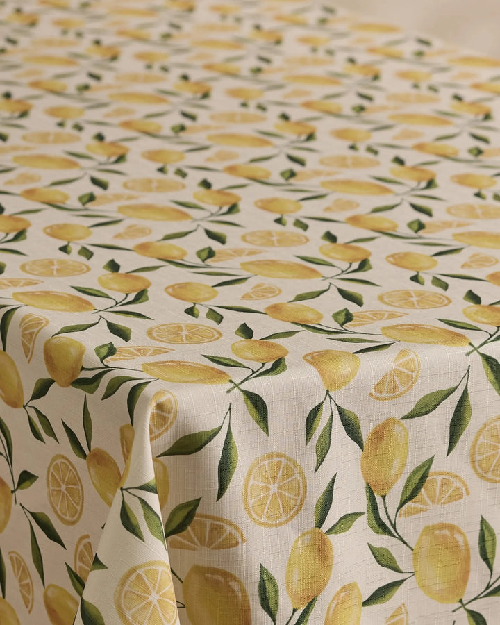 The Geometry Limoncello tablecloth has a cream background with a repeating pattern of whole lemons, lemon slices, and green leaves. Stain-resistant and stylish, its the perfect blend of function and flair for any dining space.