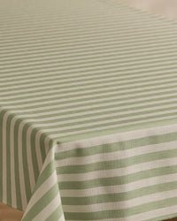 A close-up of a rectangular table covered with the Geometry Seagrass tablecloth, featuring green and white horizontal stripes on top and vertical stripes along the edge. This stain-resistant tablecloth combines style with practicality.