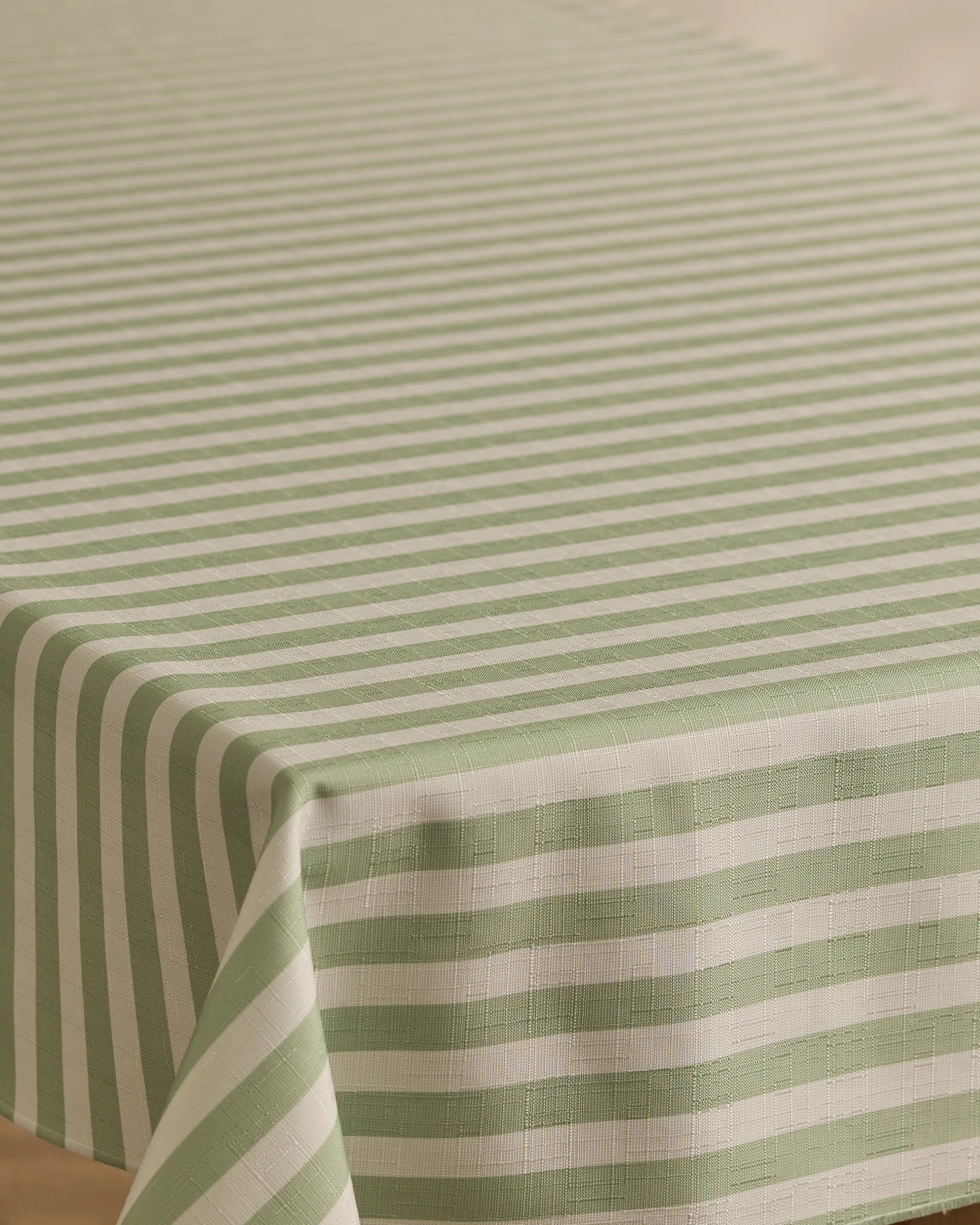 A close-up of a rectangular table covered with the Geometry Seagrass tablecloth, featuring green and white horizontal stripes on top and vertical stripes along the edge. This stain-resistant tablecloth combines style with practicality.