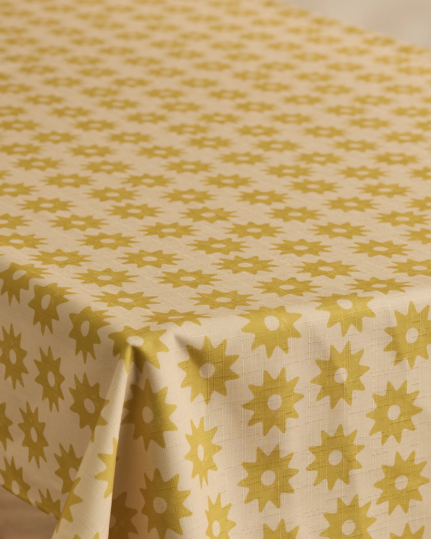 The Geometry Sunny Sun tablecloth, in beige with a repeating yellow sunburst pattern, covers a rectangular table.