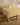 A wooden table is draped with the Geometry Sunny Sun lightweight yellow and white floral-patterned tablecloth. A white bowl of green pears sits on top, next to a wooden stool on a light wood floor.