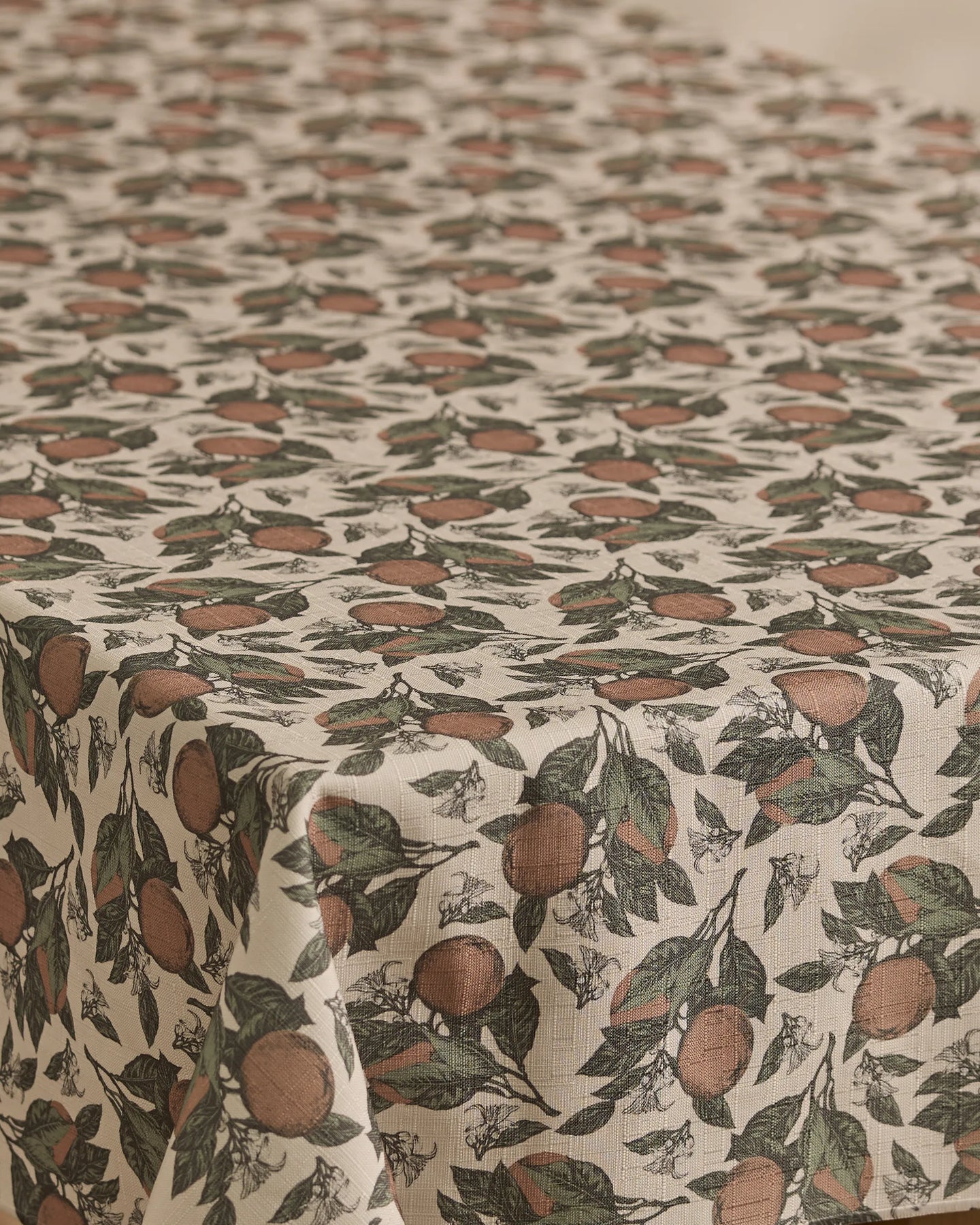 The Geometry Valencia tablecloth is lightweight and cream-colored, featuring a vintage-inspired botanical pattern of oranges and green leaves. Clusters of fruit and foliage are evenly spread across this charming, stain-resistant piece.