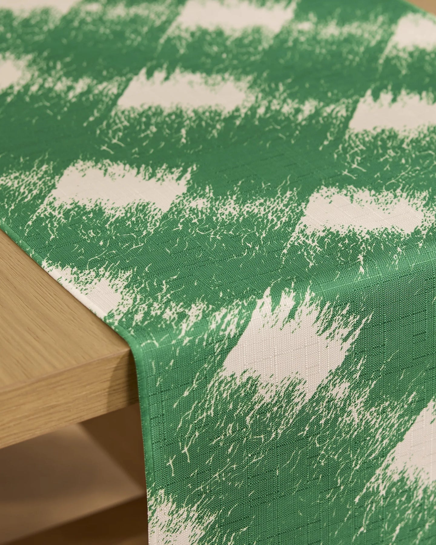 A Geometry Hairy Check Green table runner, featuring a green and white brushstroke-like pattern, is spread across a light wooden table.