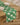A light wood dining table features Geometrys Hairy Check Green stain-resistant runner, four stacked white plates, and two forks on top, set on a wooden floor.