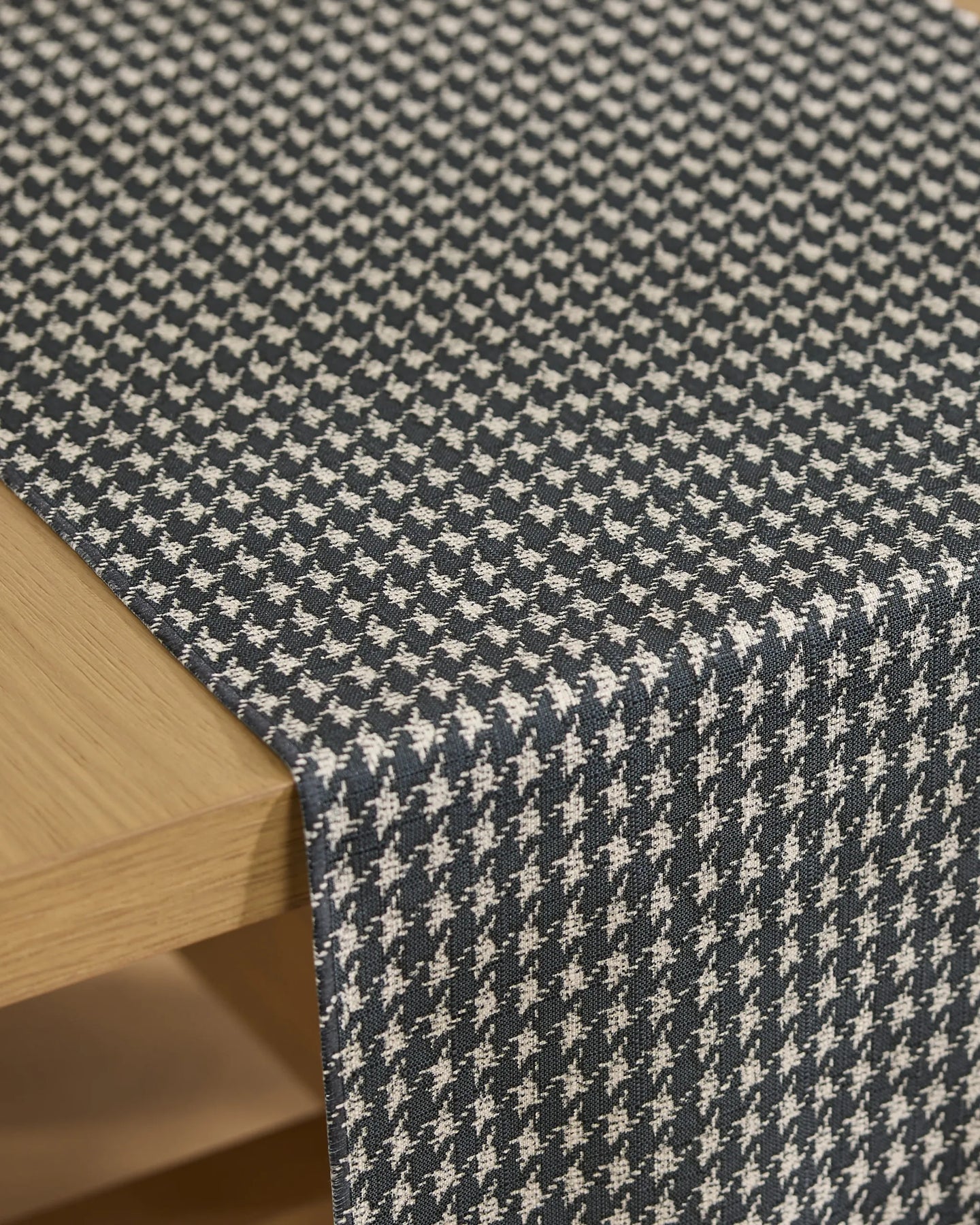 A close-up of Geometry’s Houndstooth Black stain-resistant table runner, showcasing its black and white pattern draped over a light wood table.