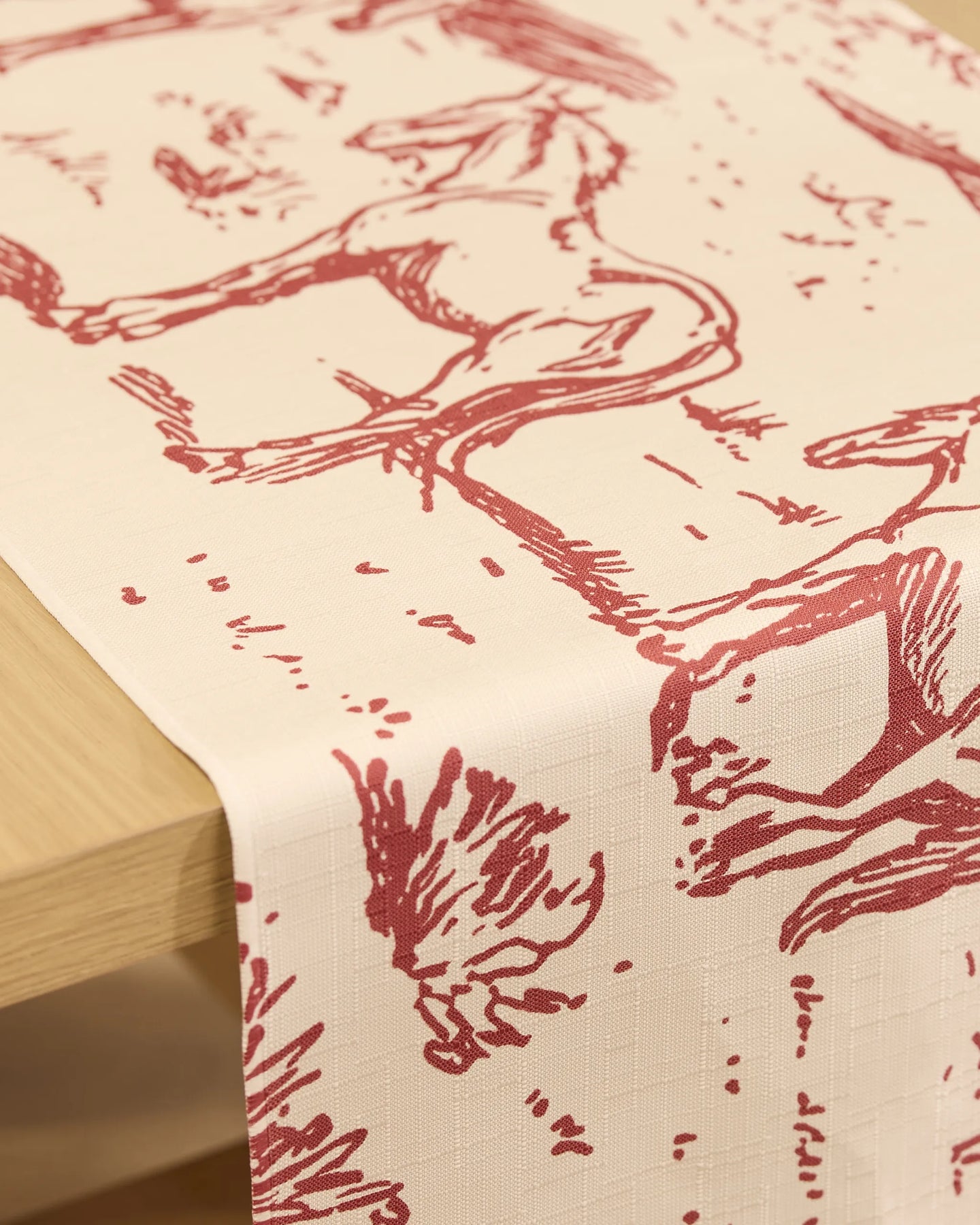 The Geometry Western Scene table runner in cream features red, sketch-style horse illustrations and is stain-resistant—perfect for draping elegantly over any wooden table.