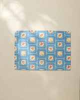 The Geometry Italian Tiles placemat features a blue geometric border and square patterns with red and yellow floral or heart motifs, arranged on a light beige surface.