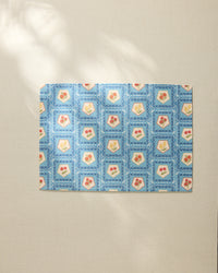 The Geometry Italian Tiles placemat features a blue geometric border and square patterns with red and yellow floral or heart motifs, arranged on a light beige surface.