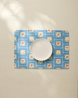 The Geometry Italian Tiles fluted plate rests on a blue floral placemat made from recycled materials atop a light tablecloth, with sunlight casting gentle shadows across the scene.