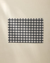 A Geometry Charcoal Gingham rectangular placemat is placed on a light beige textured surface.