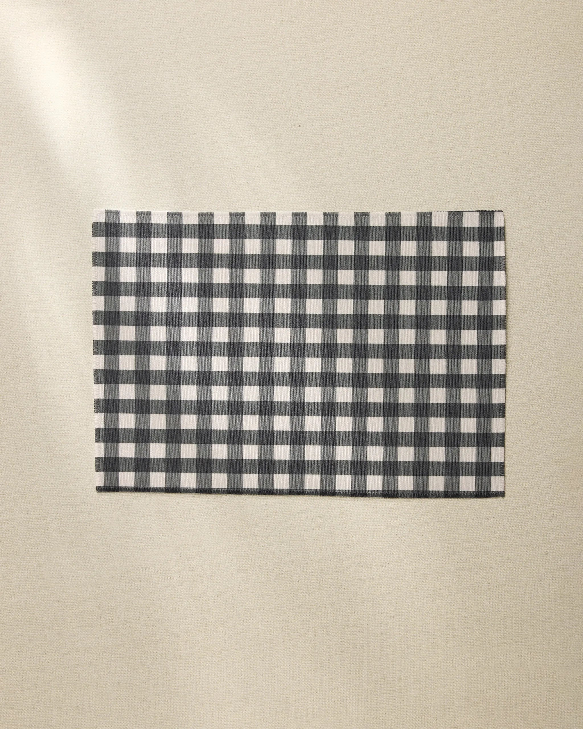 A Geometry Charcoal Gingham rectangular placemat is placed on a light beige textured surface.