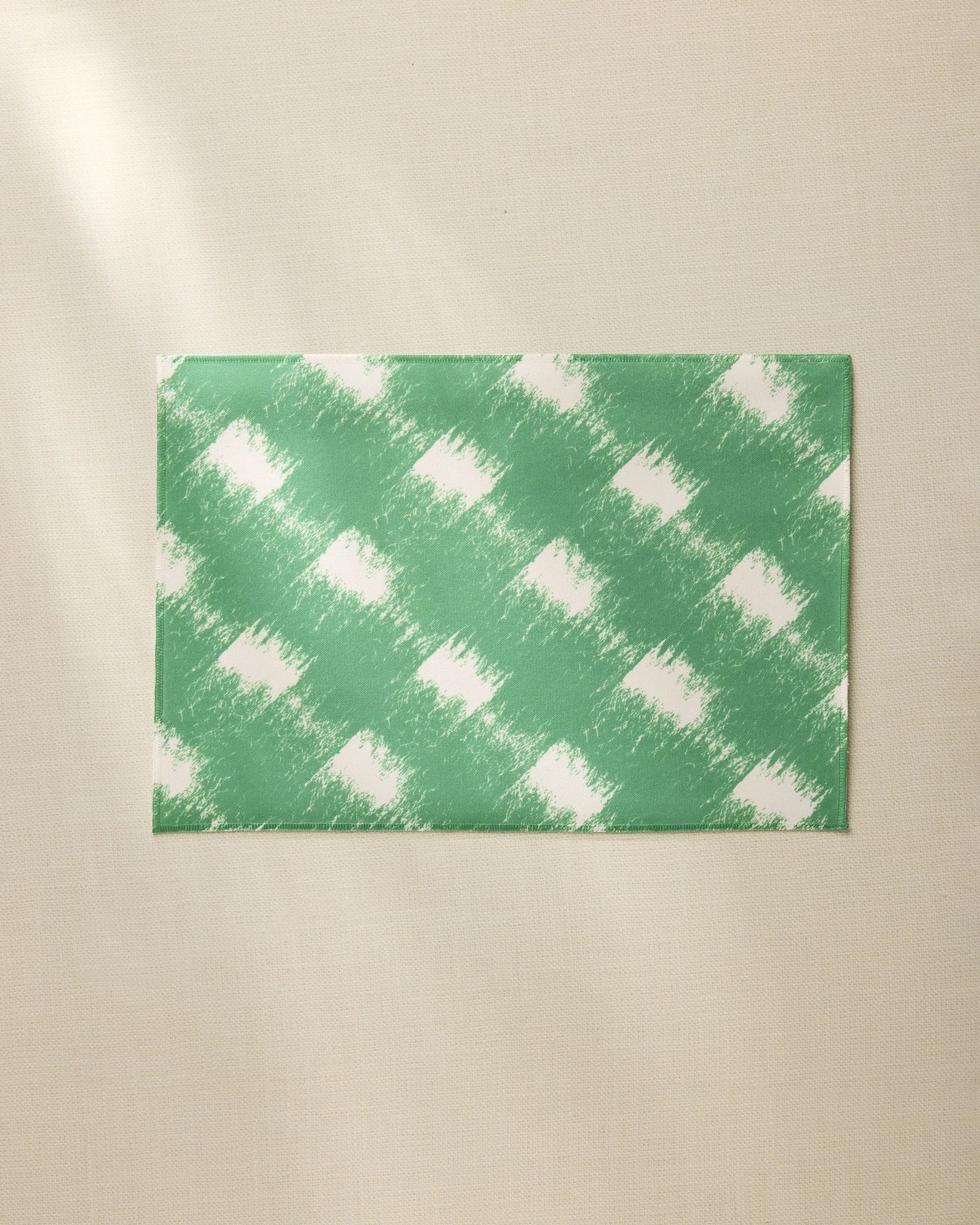 The Hairy Check Green placemat by Geometry features a white brushed checkered pattern on green, shown on a beige surface. Made from recycled materials, this everyday placemat is easy to clean and perfect for daily use.
