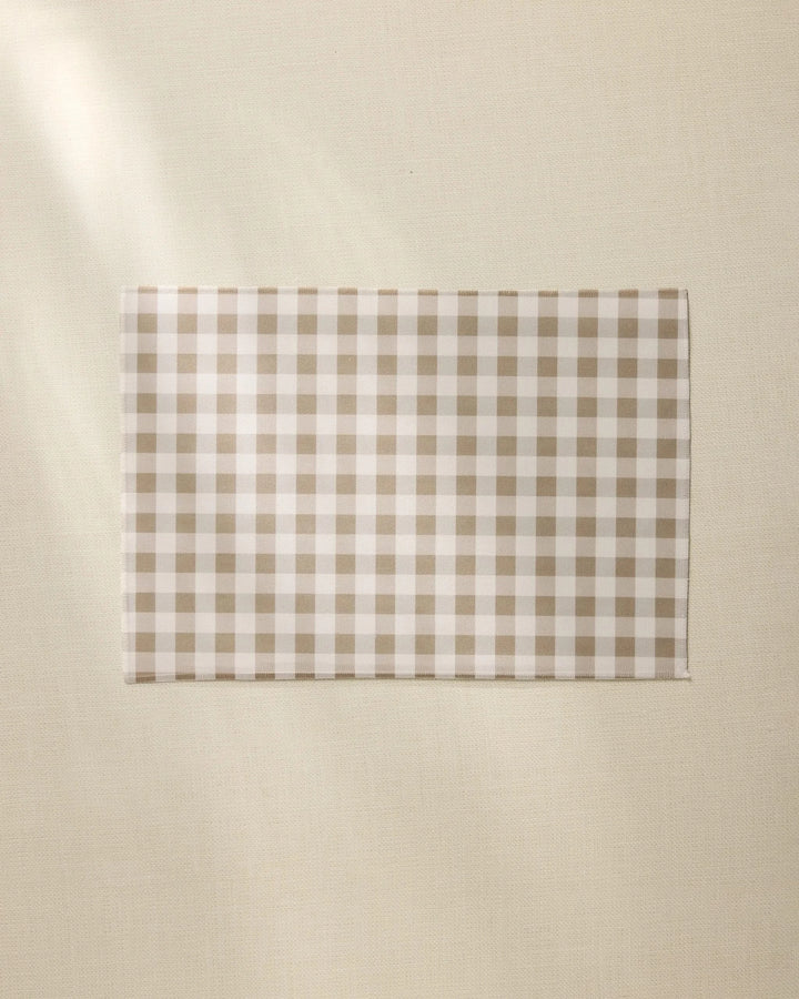 The Hazel Gingham napkin by Geometry, featuring a beige and white checkered design like our recycled placemats, is neatly displayed on a light, textured surface.
