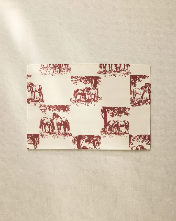 The Geometry Horse Check Cream is a rectangular, cream-colored, machine washable placemat featuring maroon horses and trees in a repeating pattern, shown on a neutral, lightly textured surface.