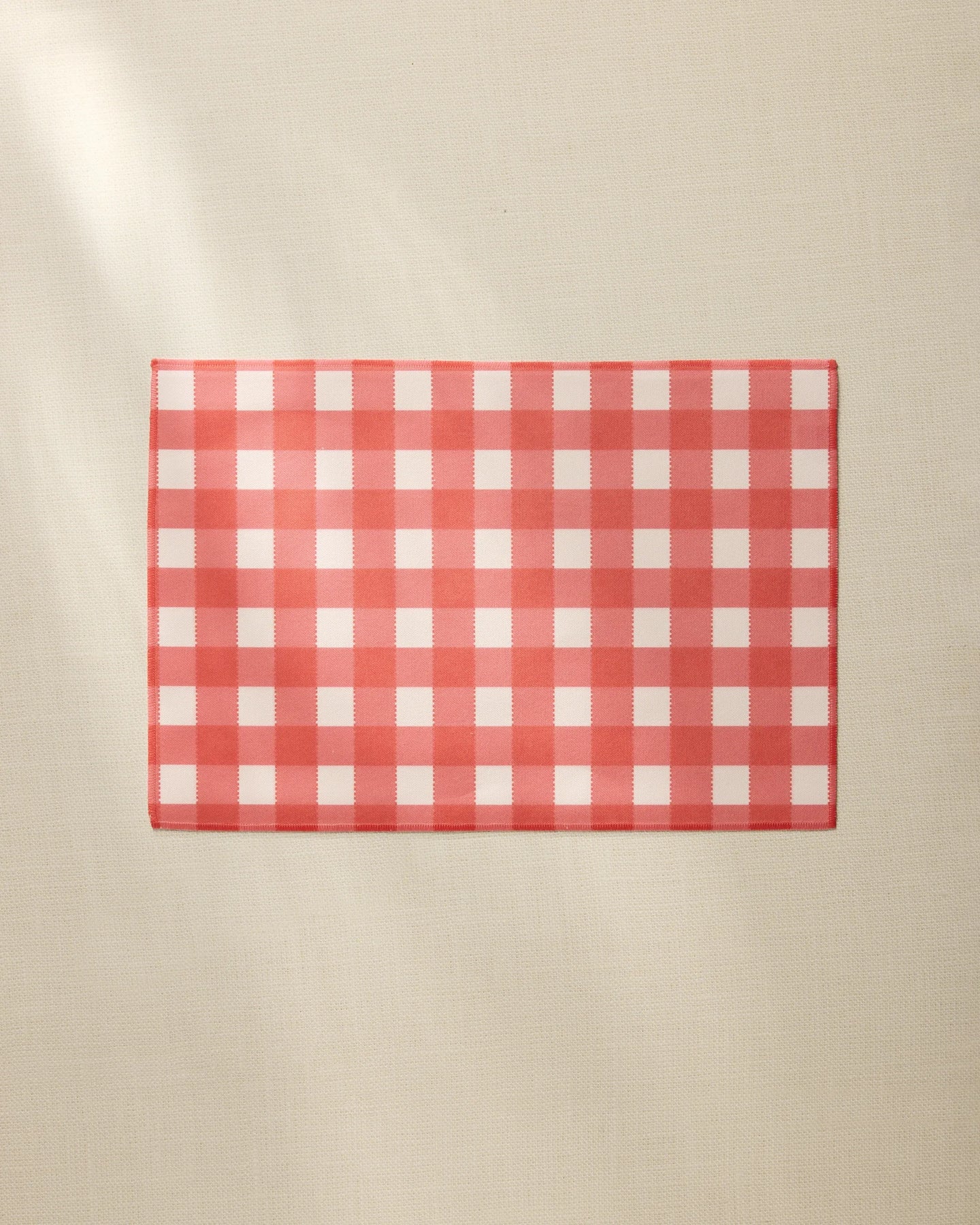 A Ripe Tomato Gingham placemat by Geometry, featuring a red and white checkered design, rests on a plain beige surface.
