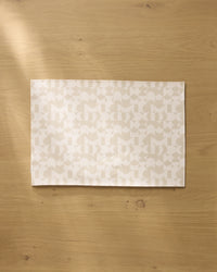 The Geometry Circle Playground placemat, with its subtle geometric design, is centered on a light wood table. Soft light casts gentle shadows, highlighting the elegant and machine washable style of these placemats.