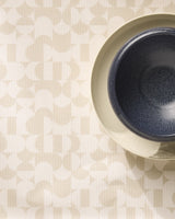 The dark blue bowl sits on a beige plate, both placed on Geometrys Circle Playground placemats—stylish, machine washable mats with a light beige geometric pattern of repeating shapes and lines.
