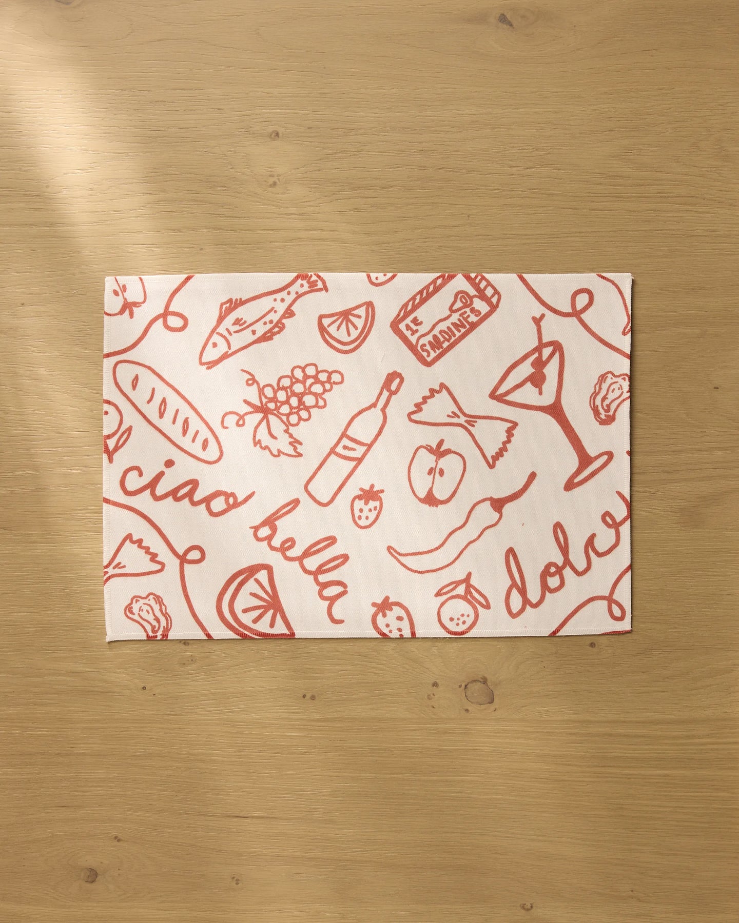 The Summer Air placemat by Geometry features red Italian-themed sketches and phrases on white recycled fabric, resting on a light wooden surface. Both stylish and practical, these placemats are machine washable.