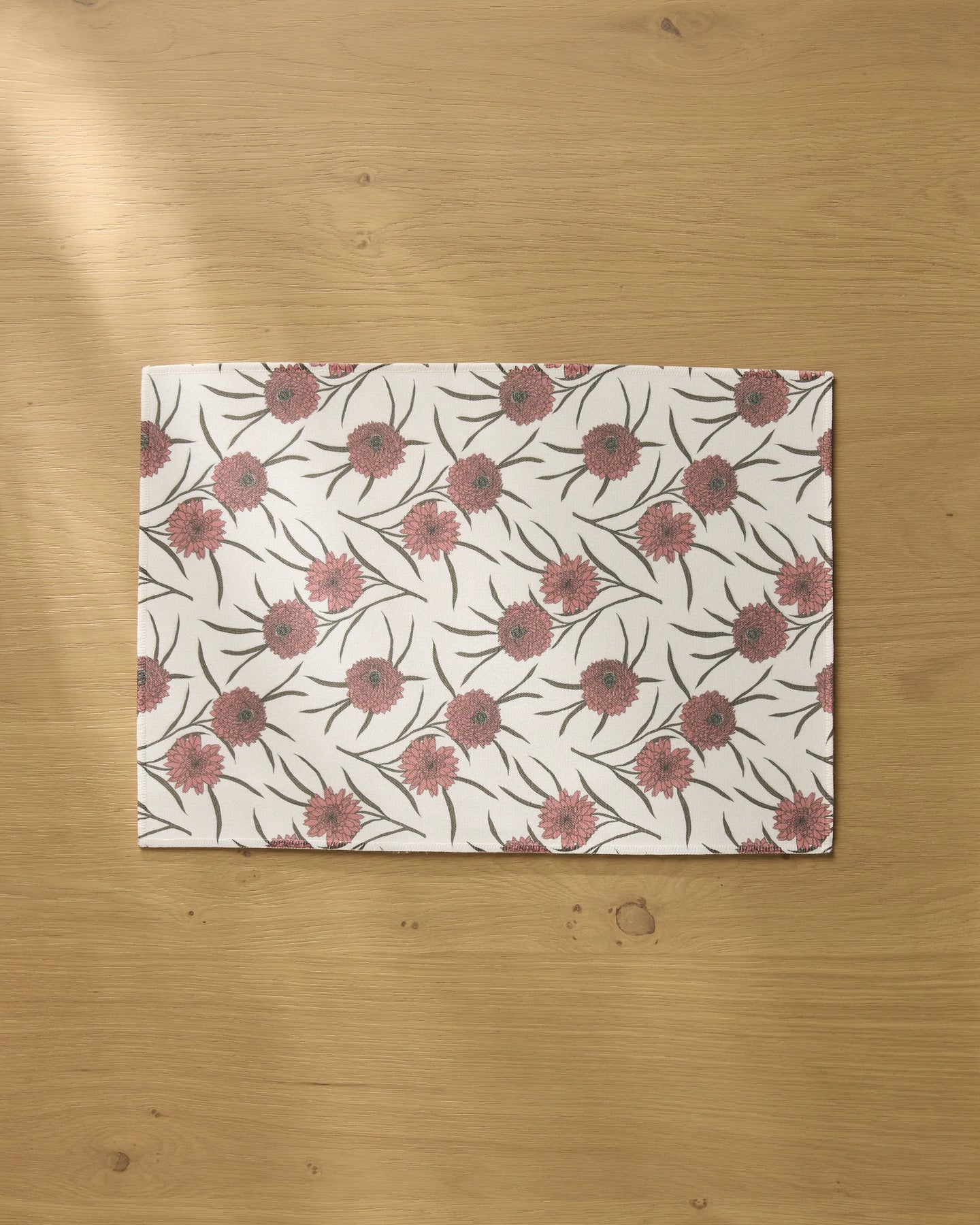 The Wild Dahlia placemat by Geometry features a pink and green floral pattern on a white background, displayed on a light wooden table.