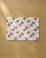 The Wild Dahlia placemat by Geometry features a pink and green floral pattern on a white background, displayed on a light wooden table.