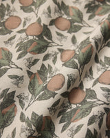 A close-up of Geometrys Valencia table runner shows its stain-resistant fabric with a botanical print of oranges, green leaves, and white blossoms on a light background. The texture and weave are clearly visible.