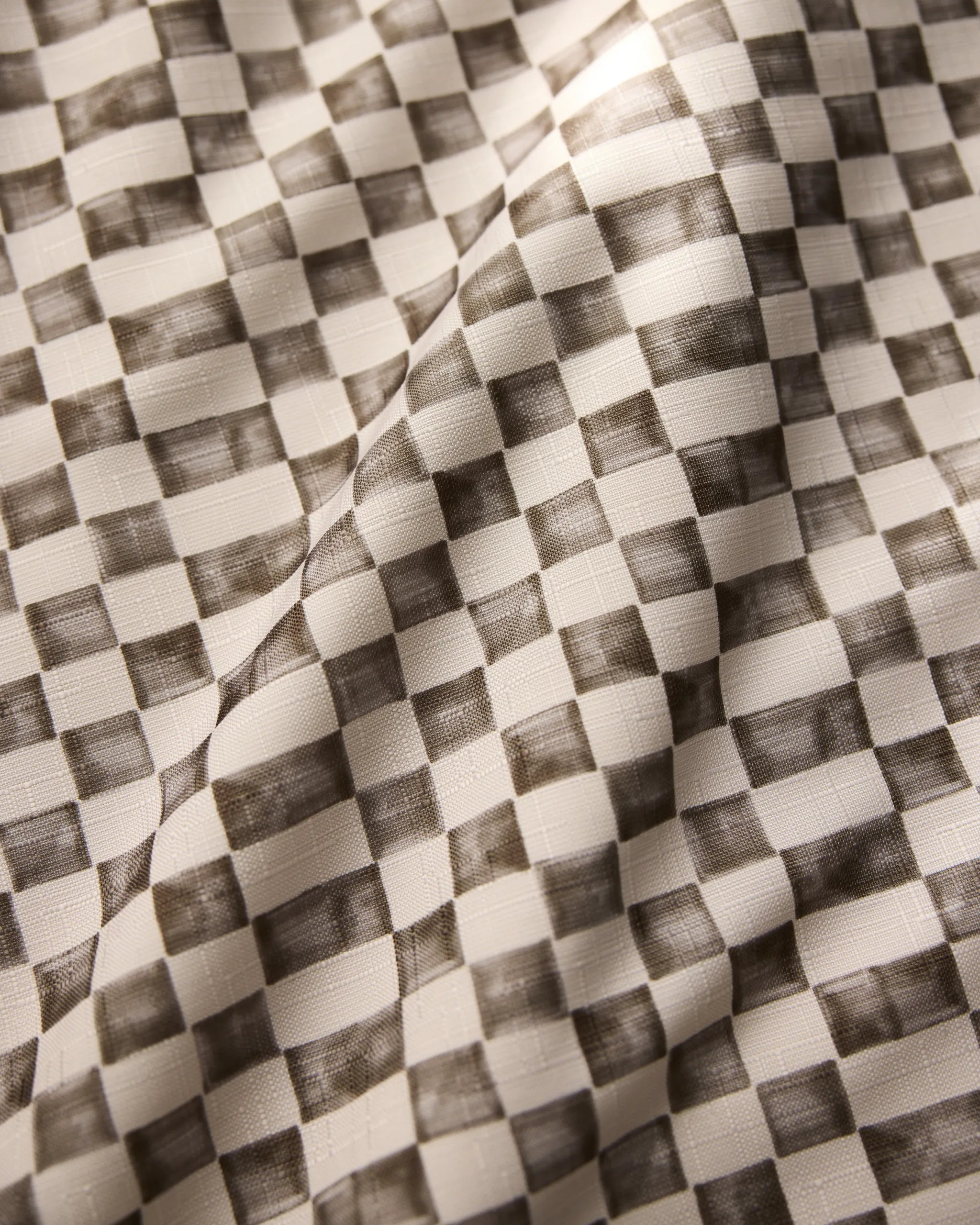 A close-up of Geometry’s Tavern tablecloth reveals a black and white checkered pattern with shaded squares; the stain-resistant fabric has visible folds and a soft, textured surface.