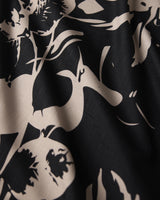 Close-up of Geometry’s Inverted Floral Black tablecloth: black recycled fabric with a beige floral pattern, featuring abstract leaves and flowers. Soft, wavy texture and a subtle grid-like weave appear in the lighter sections.