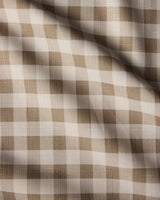 A close-up of Hazel Gingham by Geometry—a beige and white checkered fabric, softly draped to show gentle folds. Lightweight and stain-resistant, it’s perfect as an everyday tablecloth.