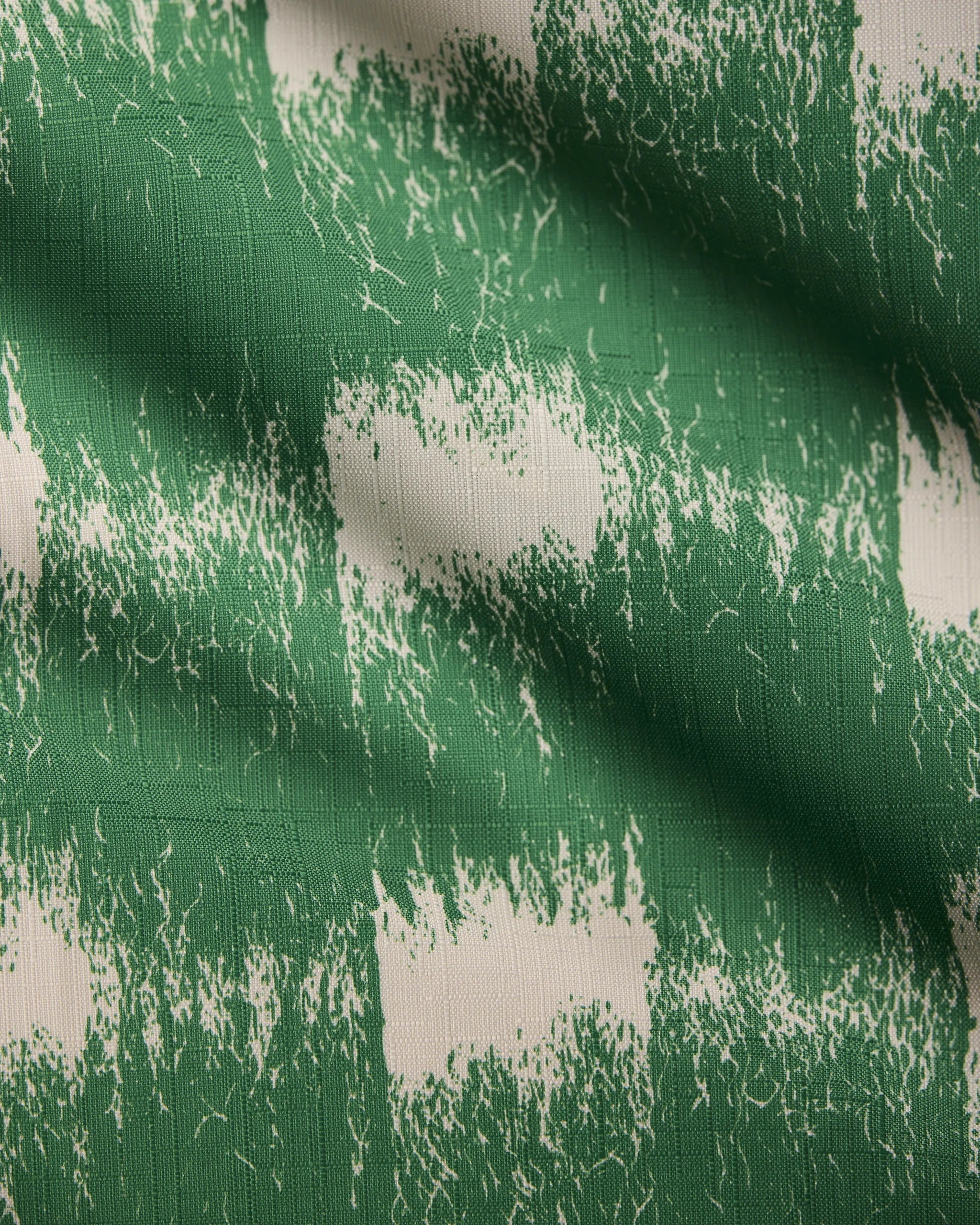 A close-up of Geometry’s Hairy Check Green table runner fabric shows its green and white rough brushstroke checkered pattern, highlighting the slight creases and texture.