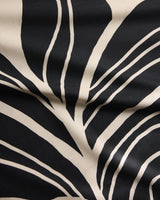 Close-up of the Geometry Giant Lush Floral tablecloth with black fabric and a bold, abstract white leaf pattern. Curved lines, organic shapes, and gentle folds highlight its sustainable woven texture.