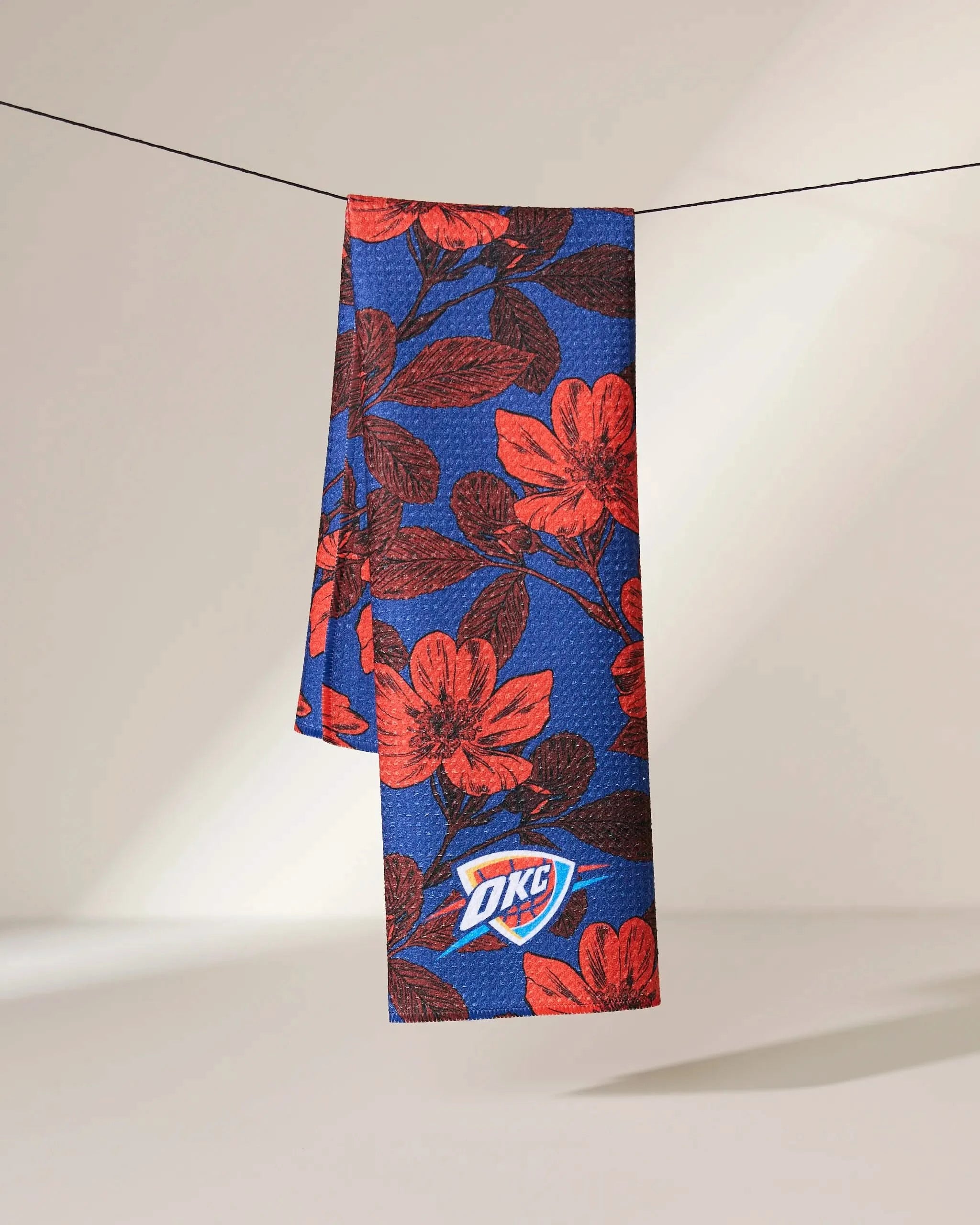 The Geometry OKC Floral towel, featuring a red floral pattern and the Oklahoma City Thunder logo, hangs against a neutral background.
