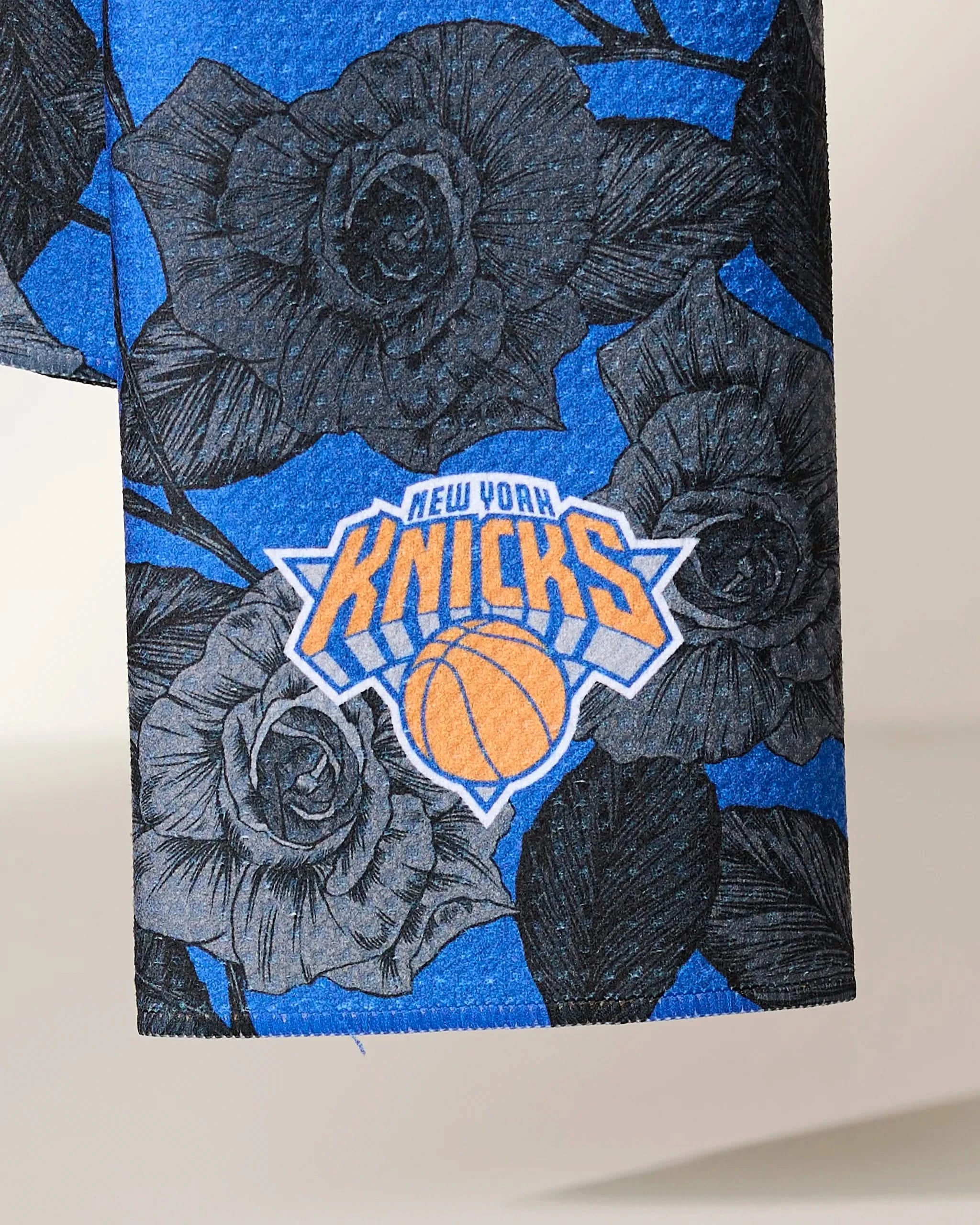 A close-up of Geometrys Knicks Floral, featuring blue fabric with black rose designs and the New York Knicks logo in orange, white, and blue.