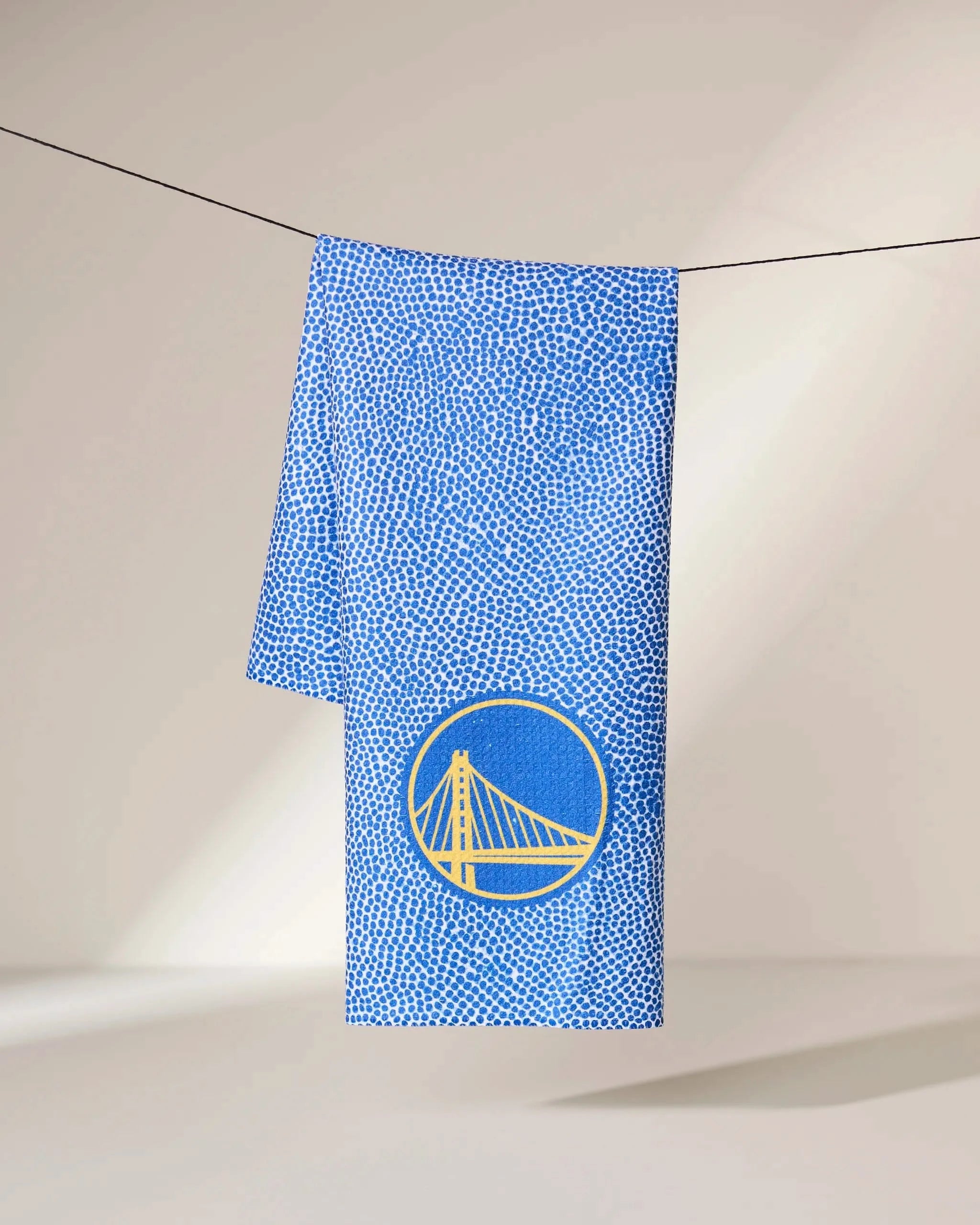 The Geometry Warriors Grip towel features blue and white speckles with a yellow circular bridge emblem, displayed on a black line against a neutral background.