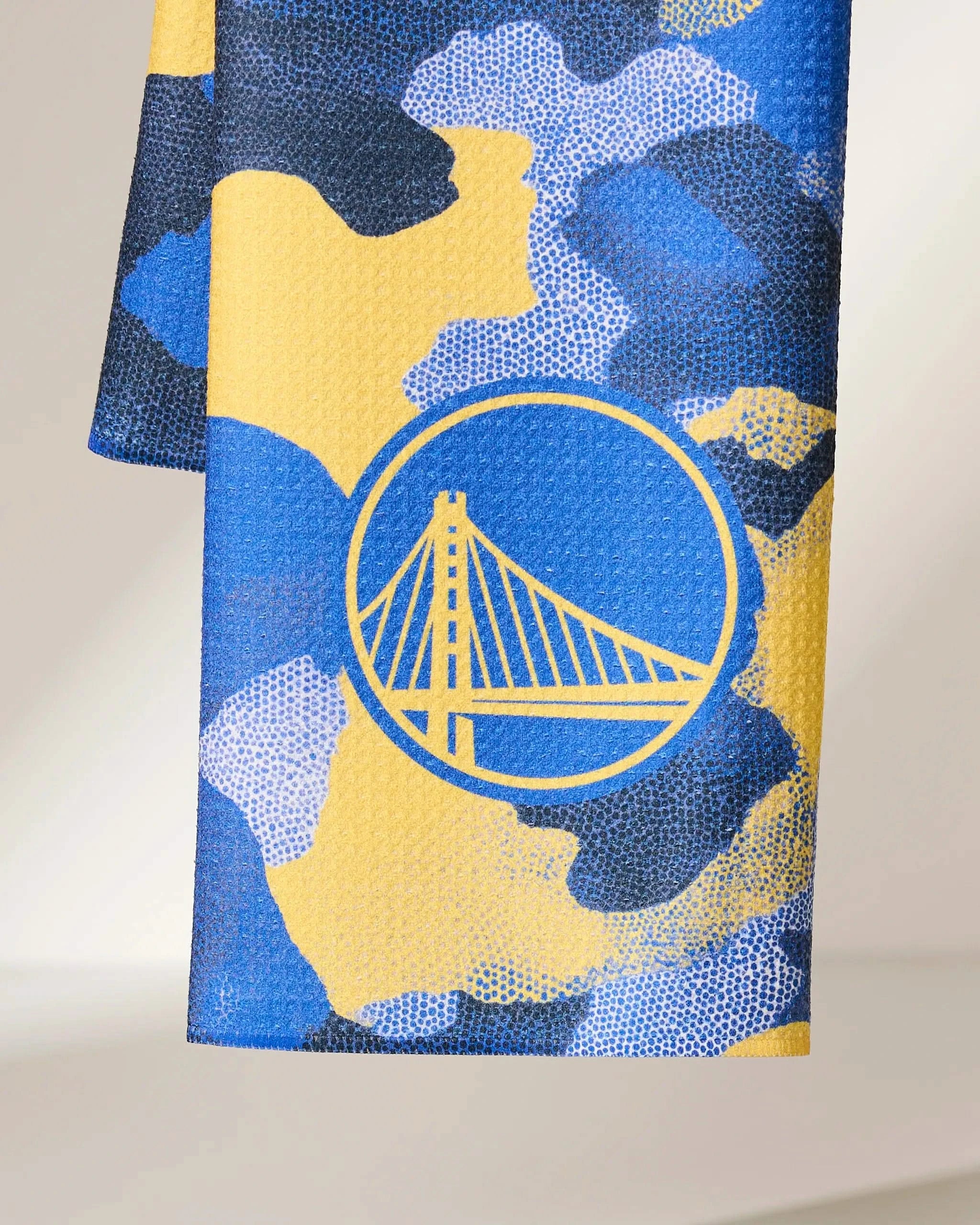 A close-up of Geometry’s Warriors Camo fabric showcases a blue, yellow, and black camouflage pattern with the Golden State Warriors bridge logo in yellow.