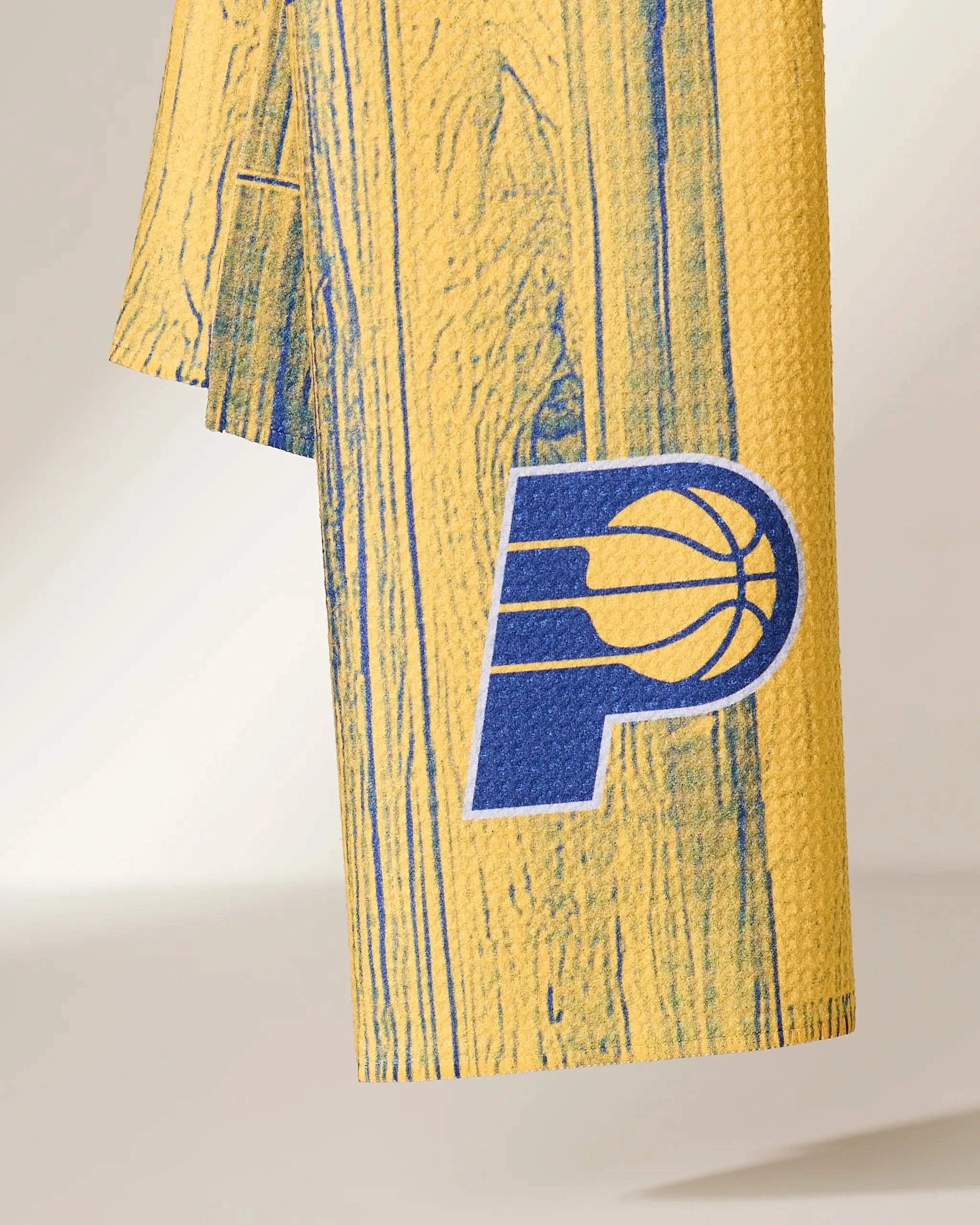 A close-up of the Pacers Zone towel by Geometry, featuring a blue Indiana Pacers basketball logo and a woodgrain pattern printed on its yellow fabric.