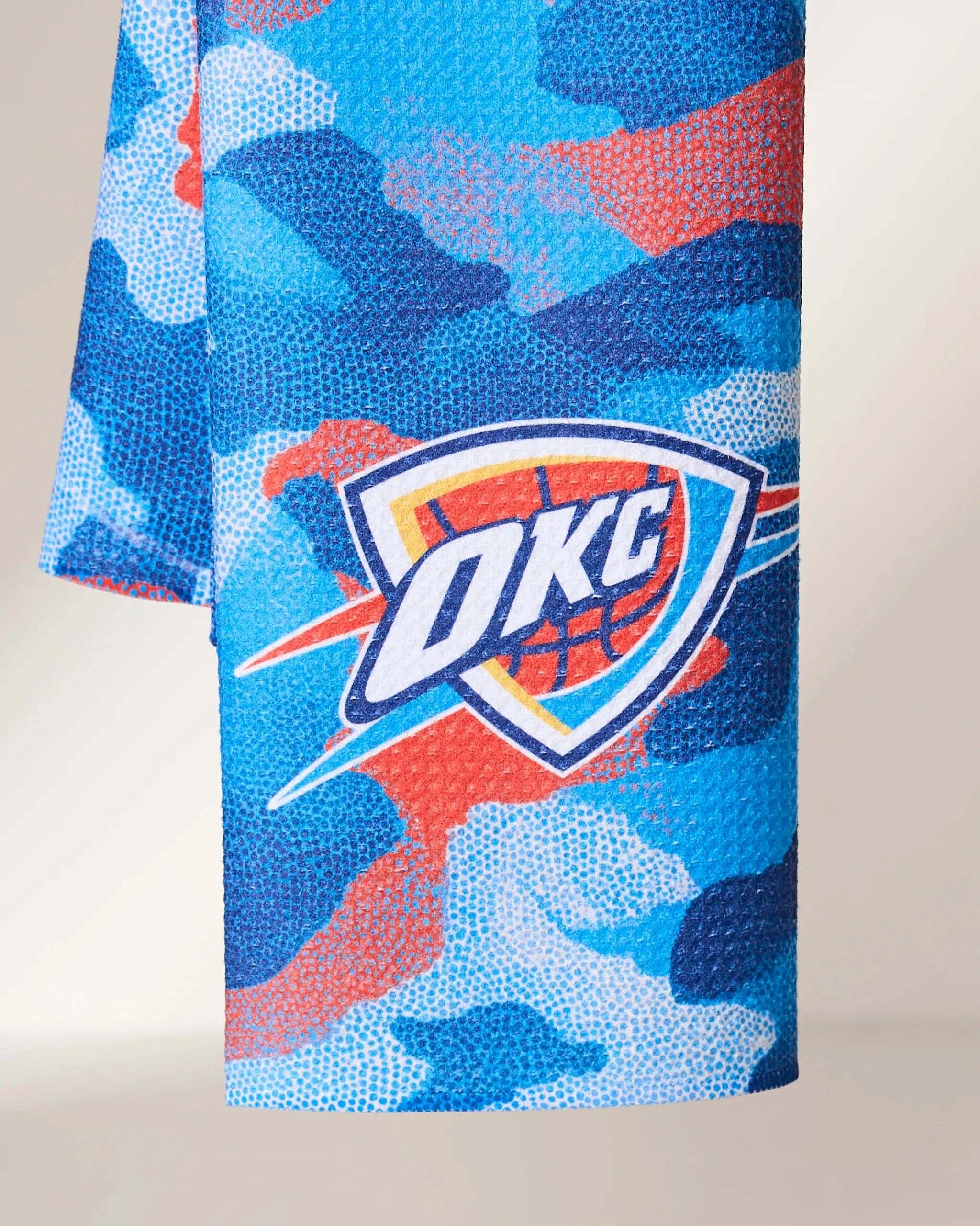 The Geometry OKC Camo towel features a blue, red, and white camouflage pattern with the Oklahoma City Thunder logo at the center.