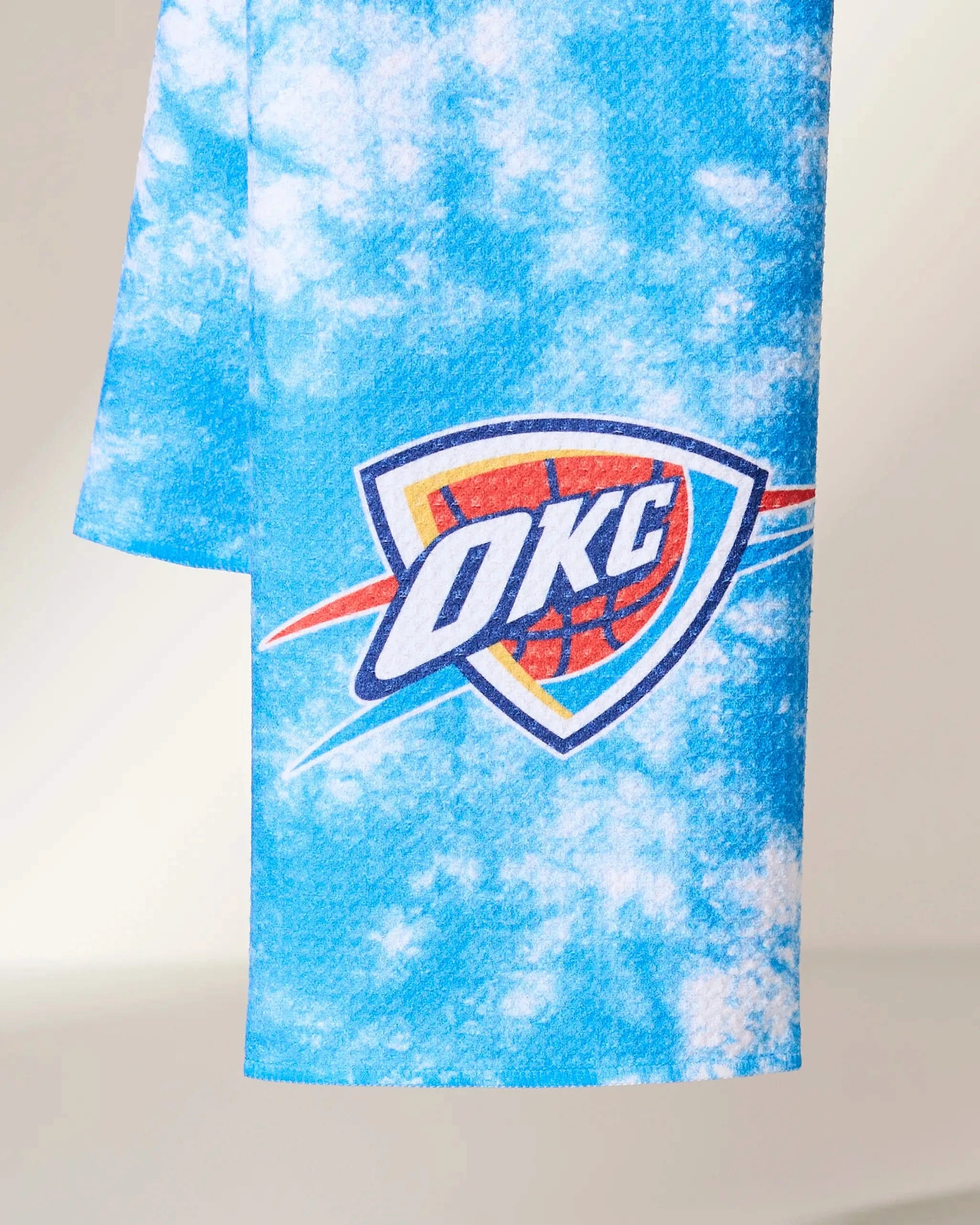 The Geometry OKC Flash towel features a blue and white tie-dye pattern with the Oklahoma City Thunder logo, showcasing an orange basketball and blue shield design.