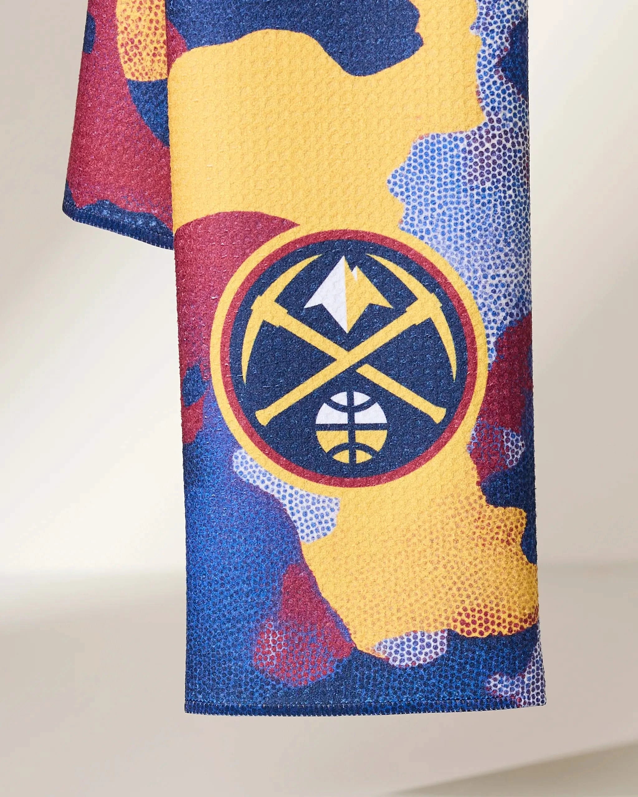 A close-up of Geometry’s Nuggets Camo fabric shows a dotted camouflage pattern in yellow, blue, red, and purple with the Denver Nuggets logo at the center.