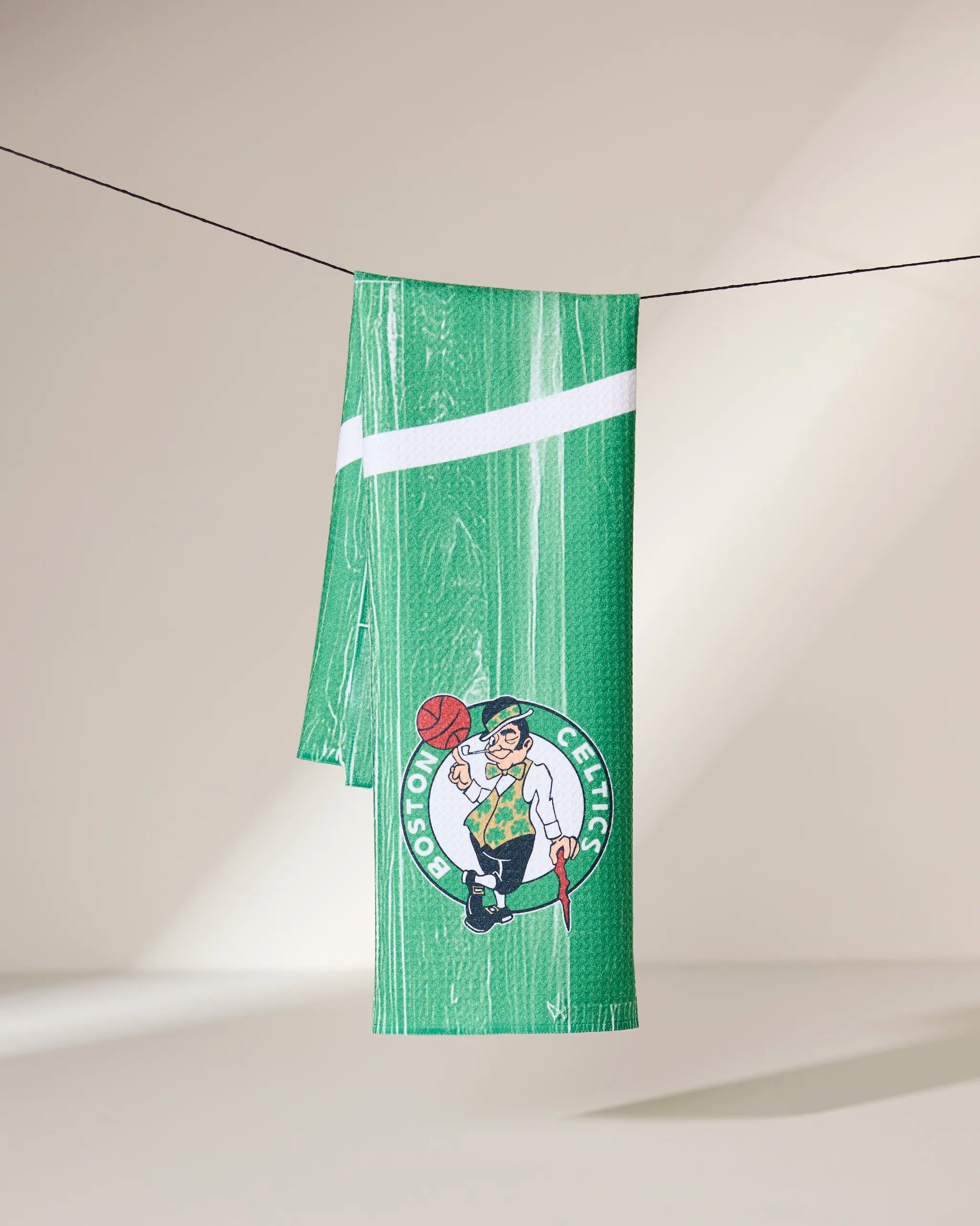 The Geometry Celtics Zone towel in green features a woodgrain pattern, white diagonal stripe, and the Boston Celtics leprechaun logo, shown hanging against a neutral background.