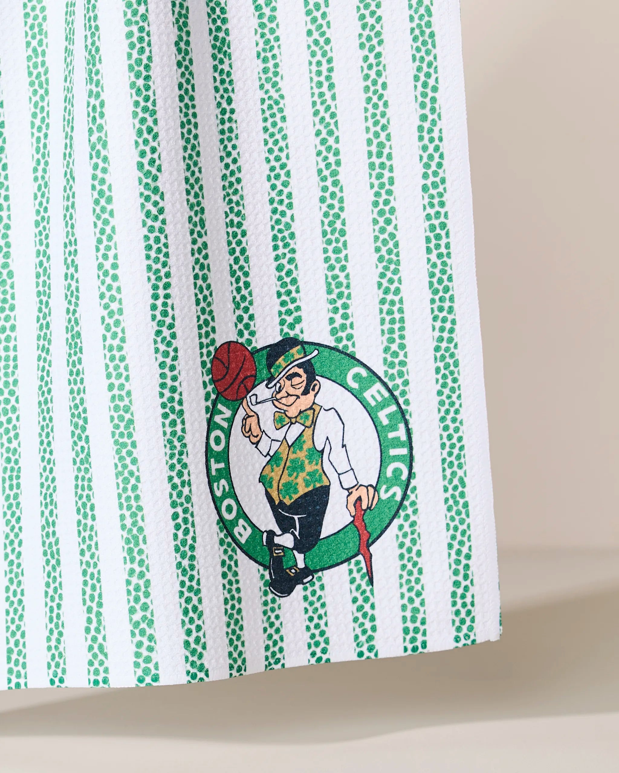 The Geometry Celtics Grip Stripe features green and white vertical stripes with the Boston Celtics leprechaun logo spinning a basketball inside a green circle with the team’s name.