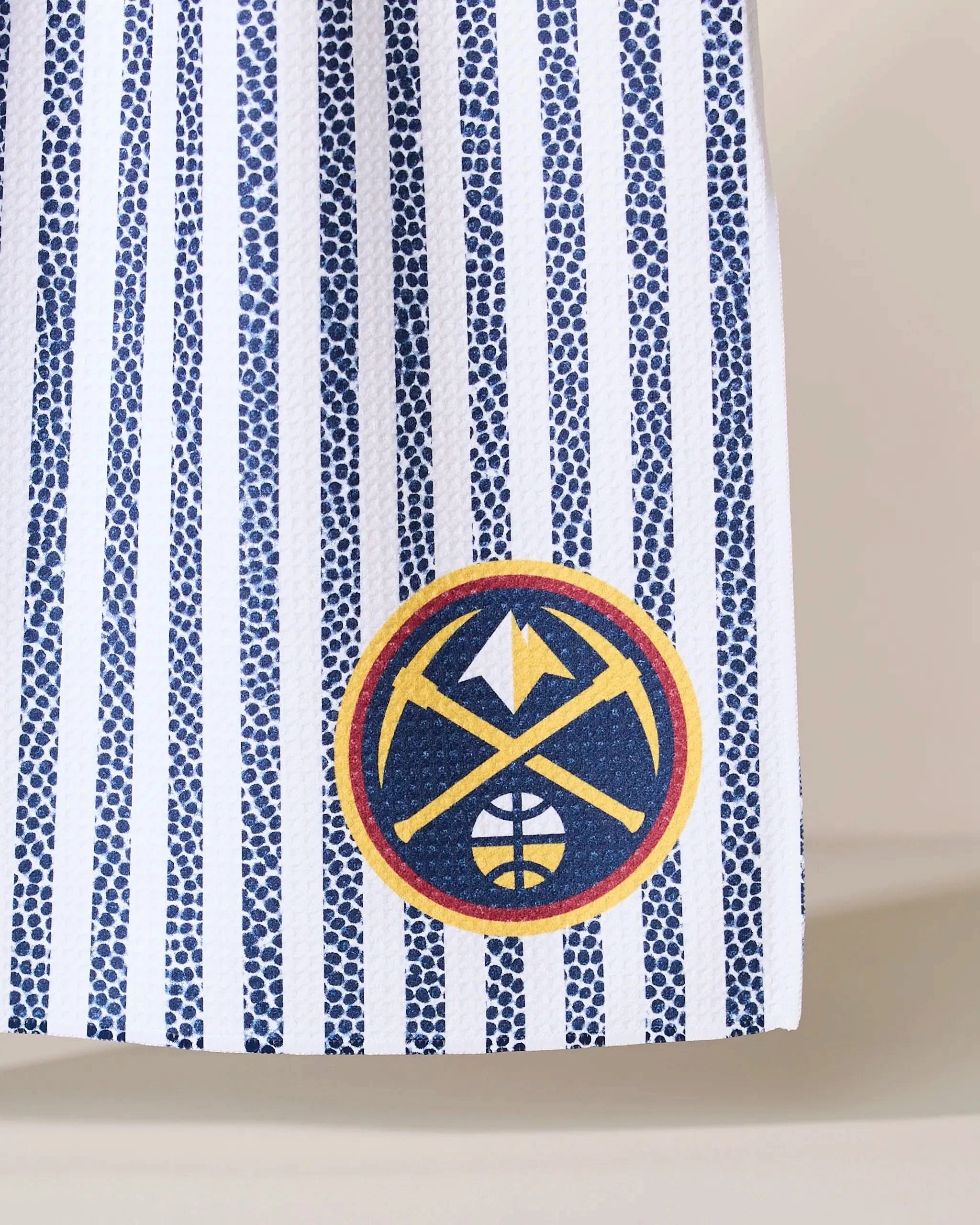 A close-up of Geometry’s Nuggets Grip Stripe fabric, featuring vertical blue and white stripes with the Denver Nuggets logo in the bottom right corner.