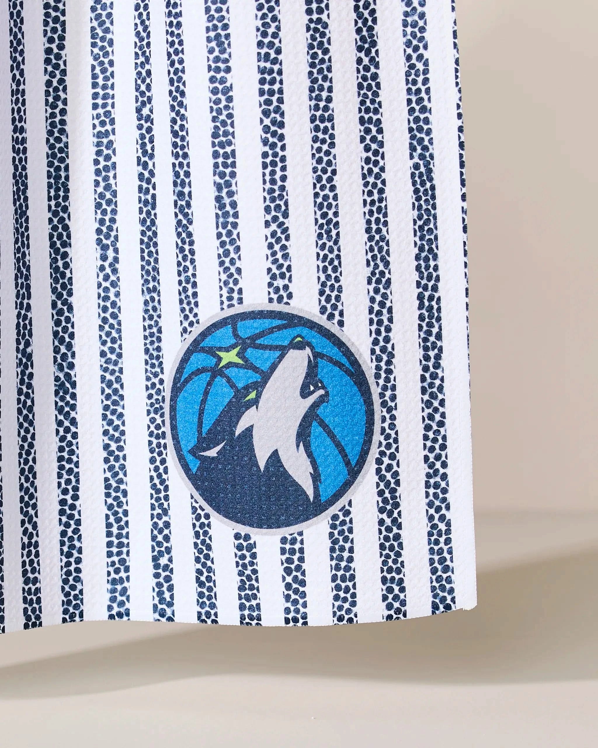 Close-up of Geometrys Timberwolves Grip Stripe fabric, showcasing vertical navy blue and white stripes with the Minnesota Timberwolves logo—a howling wolf on a starry basketball background—printed near the bottom.