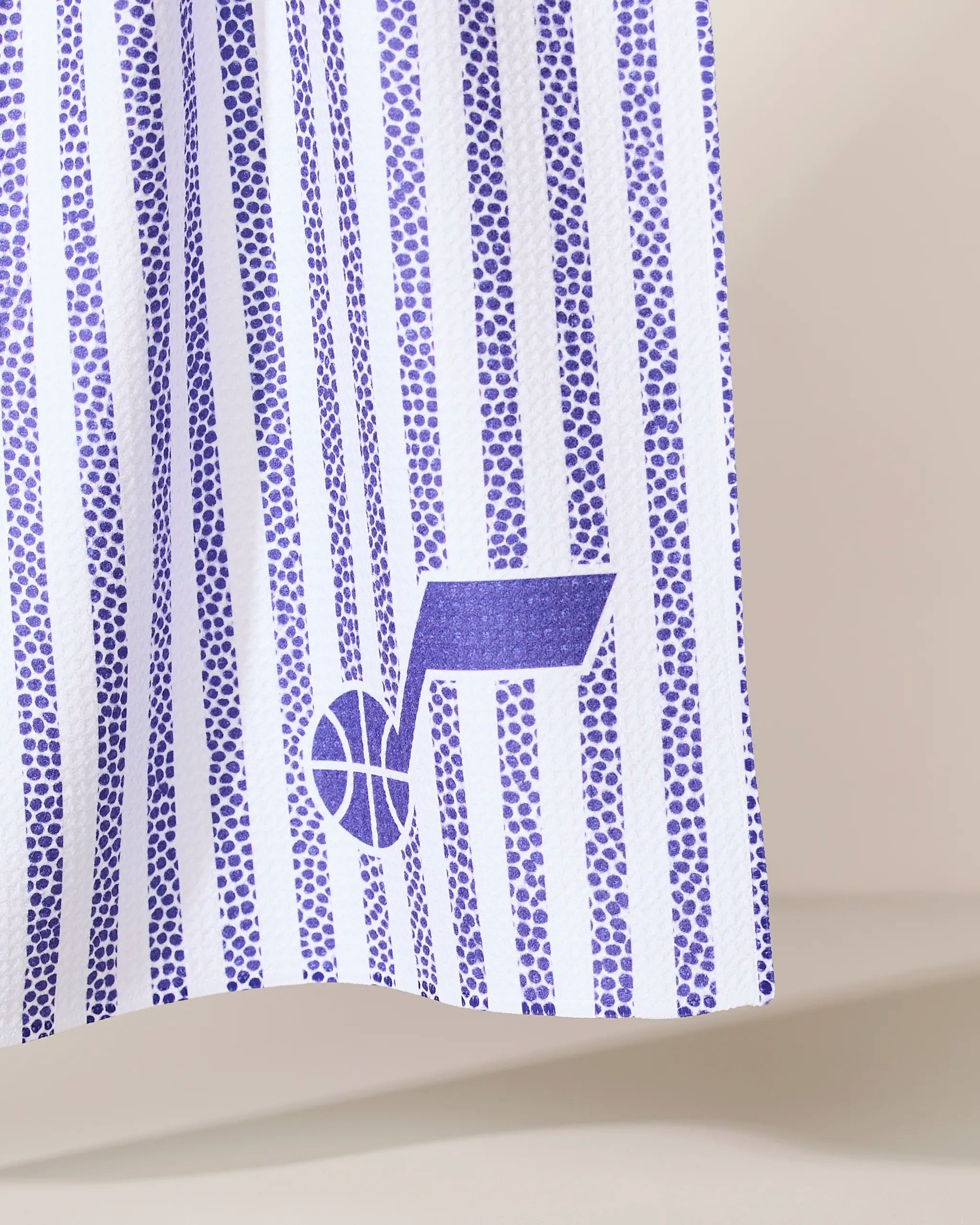 A close-up of the Jazz Grip Stripe fabric by Geometry, showing vertical purple and white stripes with a purple Utah Jazz basketball logo near the bottom right.
