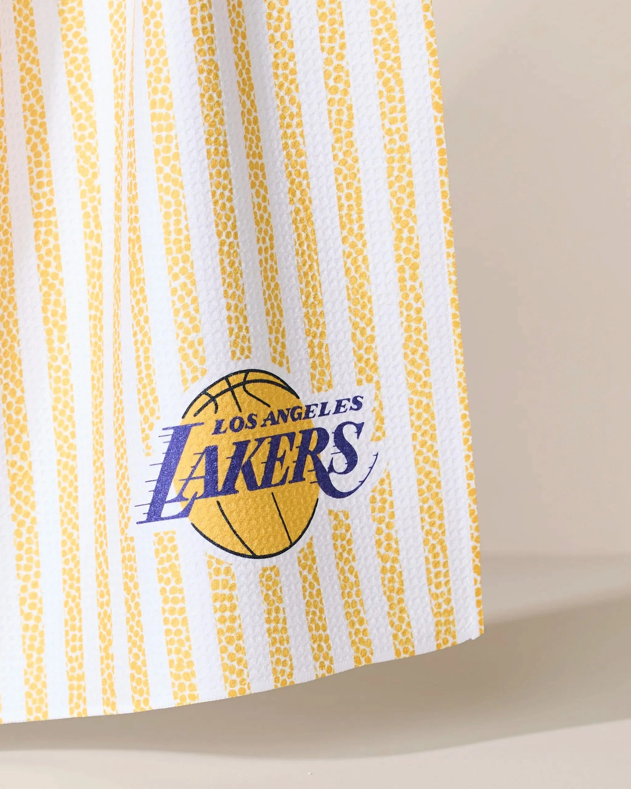 The Lakers Grip Stripe by Geometry features vertical yellow and white stripes with the Los Angeles Lakers logo—a purple and gold basketball design with the team name—inspired by classic team colors.