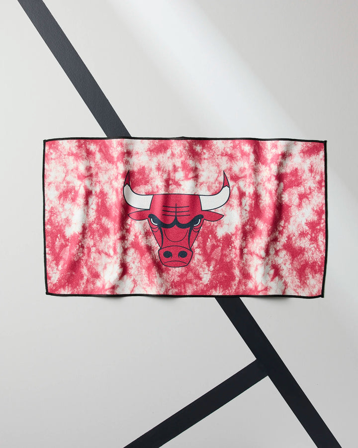 The Bulls Flash fitness towel by NBALAB x Geometry, featuring a red and white tie-dye design and the Chicago Bulls logo, is displayed flat on a light surface with two bold dark diagonal lines crossing it.